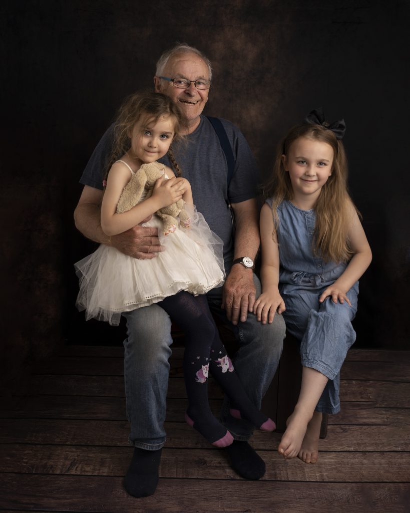 Grandad and his grandaughters sitting together by Family photographer Suffolk