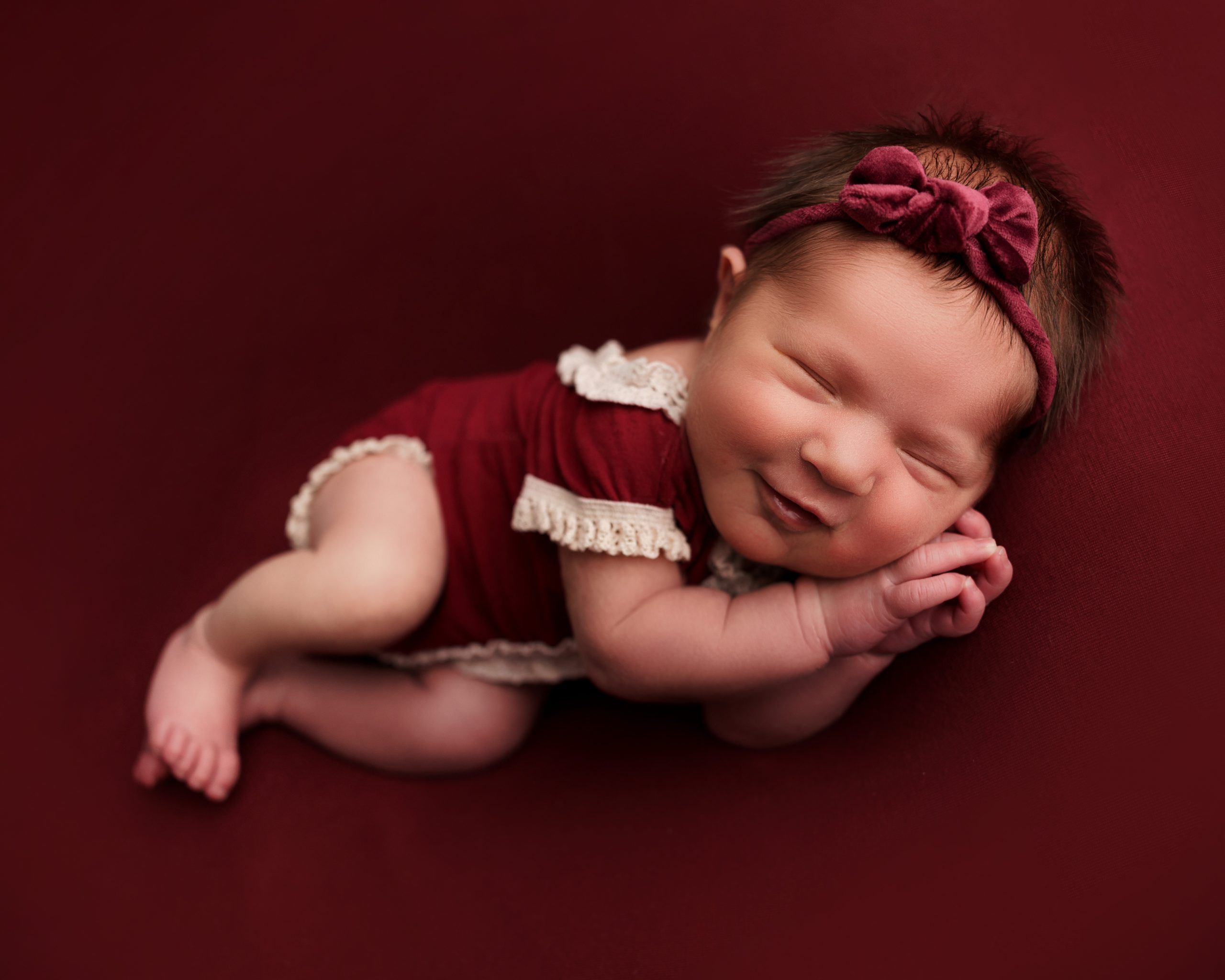 newborn baby girl dressed in red smiling by the cow shed studio